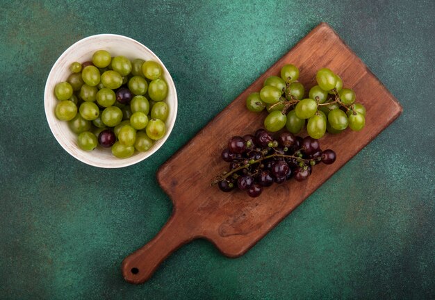 Vista superior das uvas na tábua com bagas de uva em uma tigela sobre fundo verde