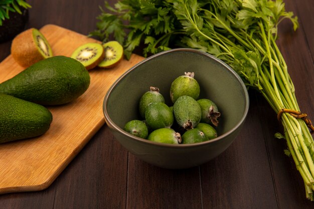 Vista superior de abacates em formato de pêra em uma mesa de cozinha de madeira com fatias de kiwi com feijoas em uma tigela com salsa isolada em uma superfície de madeira