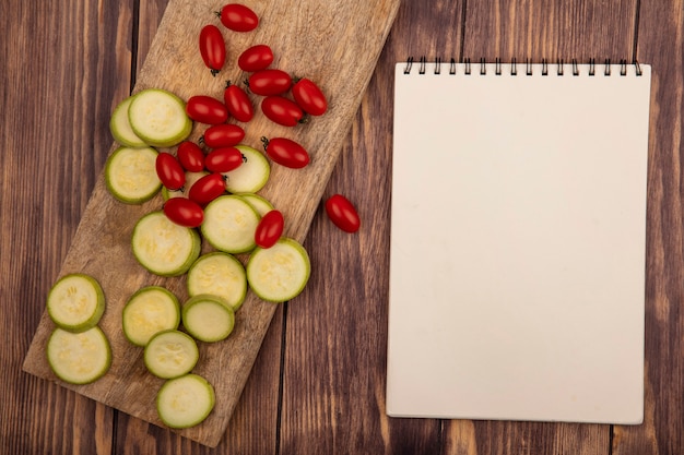 Vista superior de abobrinhas picadas ricos em vitaminas em uma placa de cozinha de madeira com tomates cereja em um fundo de madeira com espaço de cópia