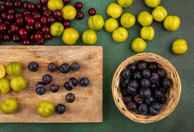 Vista superior de abrigos com ameixas de cereja verdes em uma cozinha de madeira com cerejas vermelhas e ameixas de cereja verdes isoladas em um fundo verde