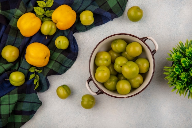 Foto grátis vista superior de ameixas de cereja verdes em uma tigela com pêssegos frescos e ameixas de cereja isoladas em um pano xadrez em um fundo branco