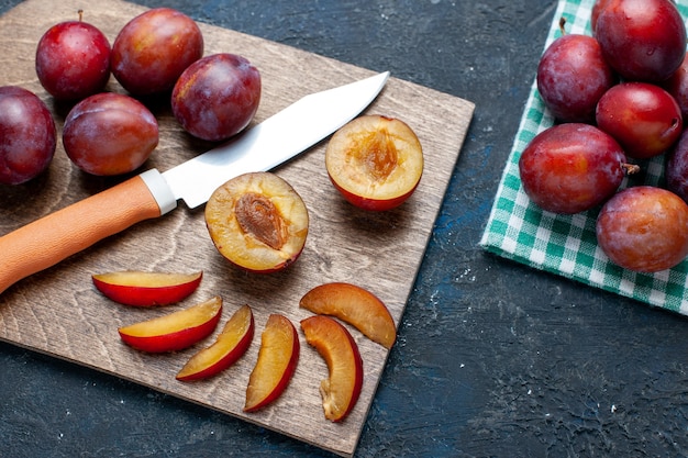 Vista superior de ameixas frescas inteiras maduras e suculentas cortadas em uma mesa cinza-escura, frutas com vitaminas frescas no verão