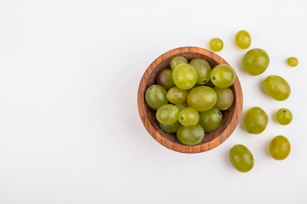 Vista superior de bagas de uvas brancas em uma tigela e no fundo branco com espaço de cópia