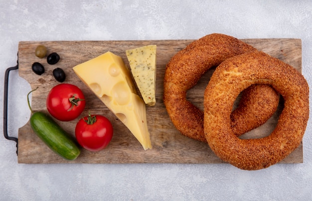 Foto grátis vista superior de bagels turcos de gergelim em uma mesa de cozinha de madeira com azeitonas, queijo, pepinos e tomates em um fundo branco