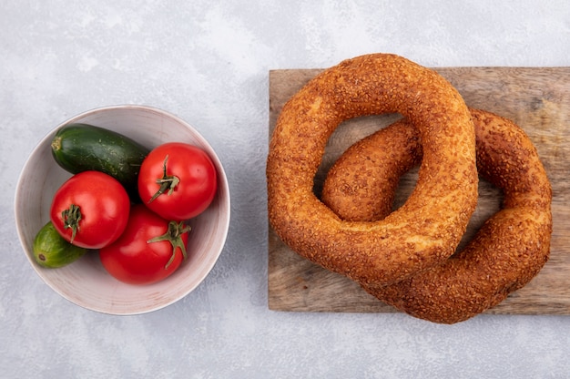 Foto grátis vista superior de bagels turcos tradicionais em uma mesa de cozinha de madeira com uma tigela de tomates e pepinos em um fundo branco