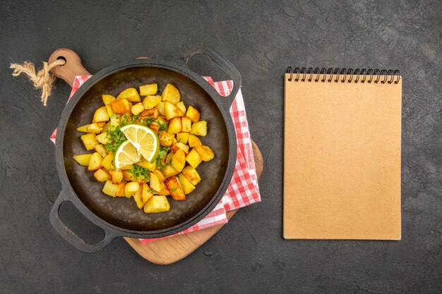 Vista superior de batatas fritas dentro de uma panela com verduras e limão na mesa escura