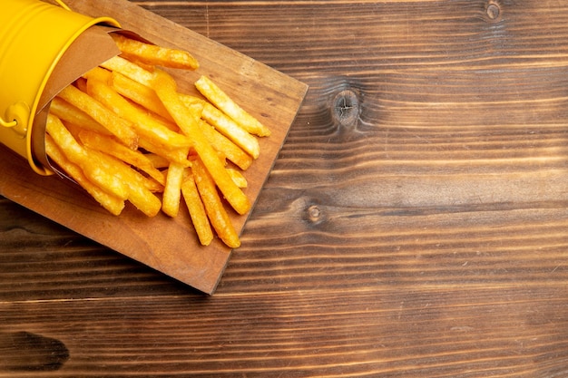 Vista superior de batatas fritas dentro de uma pequena cesta na mesa marrom