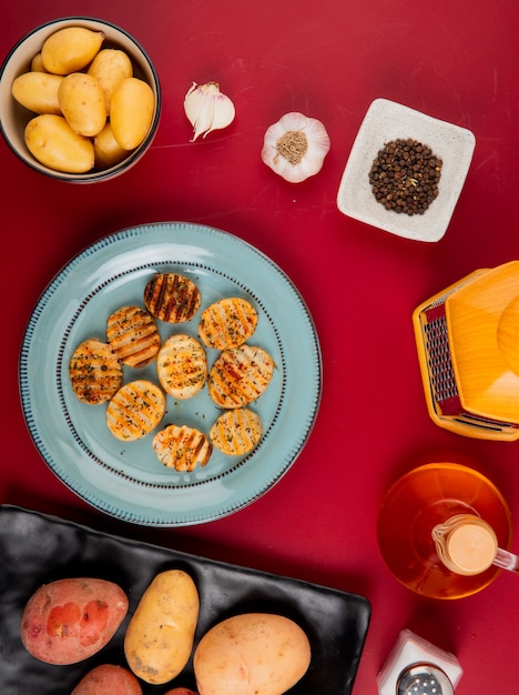 Foto grátis vista superior de batatas fritas e não cozidas em pratos e tigela com ralador de alho manteiga pimenta na mesa de bordo