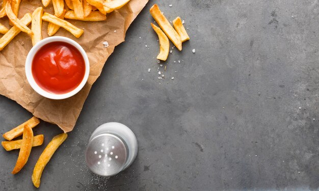 Vista superior de batatas fritas no papel com sal e ketchup