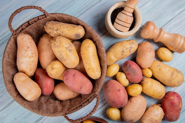 Foto grátis vista superior de batatas na cesta com pimenta preta sementes sal e outras batatas na superfície de madeira