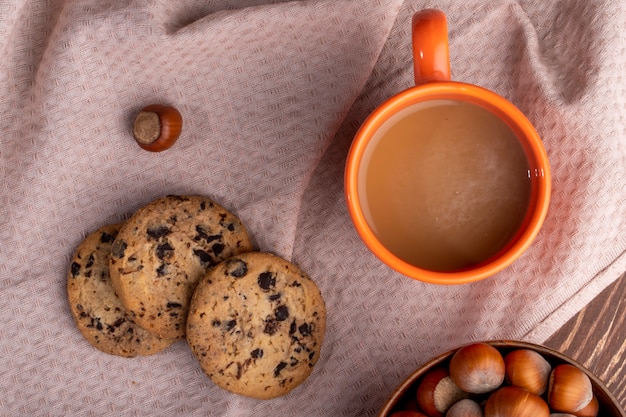 Vista superior de biscoitos de aveia com gotas de chocolate e uma caneca de bebida de cacau numa toalha de mesa