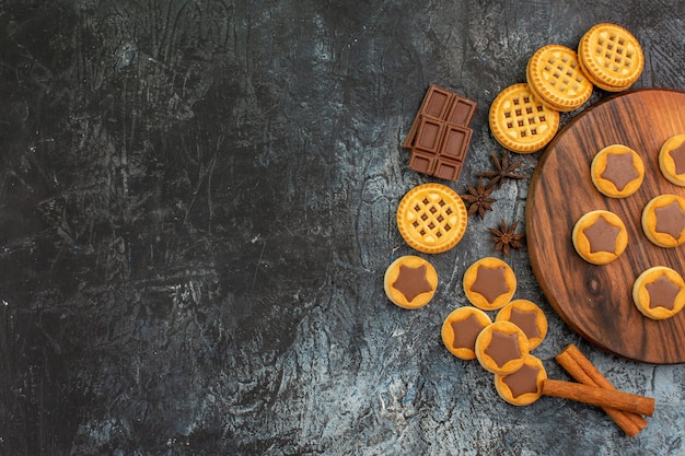 Vista superior de biscoitos em uma travessa de madeira com anis, chocolate e canela em fundo cinza