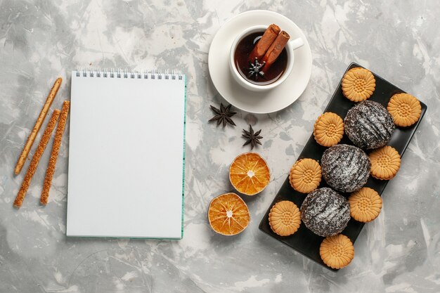 Vista superior de bolos de chocolate com biscoitos e uma xícara de chá em uma superfície branca clara