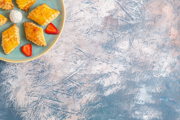 Vista superior de bolos doces deliciosos com morangos na mesa azul