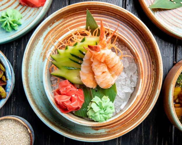 vista superior de camarão com pepino fatiado e gengibre na folha de bambu em cubos de gelo em um prato na mesa