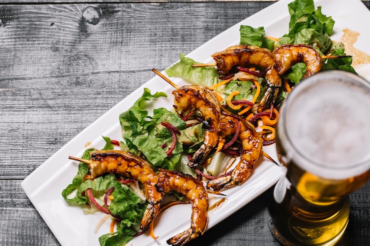 Foto grátis vista superior de camarão grelhado no palito com folhas de salada e um copo de cerveja