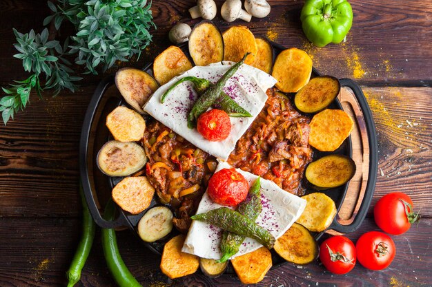 Vista superior de carne com berinjela, tomate, batata, pão pita cogumelos e pimenta em um prato redondo horizontal