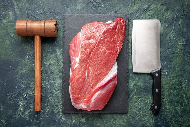 Vista superior de carne crua vermelha fresca em uma tábua de corte, martelo de madeira e machado em fundo de cor verde e preto