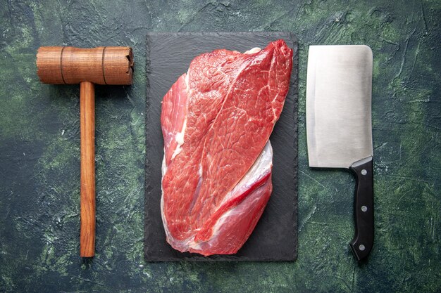 Vista superior de carne crua vermelha fresca em uma tábua de corte, martelo de madeira e machado em fundo de cor verde e preto