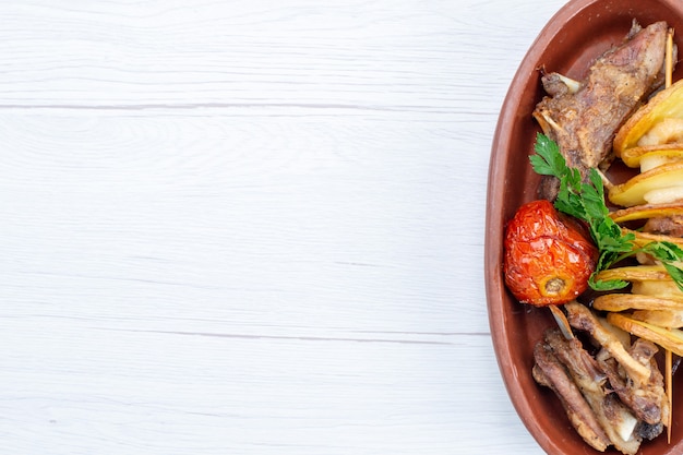 Vista superior de carne frita com verduras e ameixas assadas dentro de um prato marrom na mesa de luz, refeição de comida prato de carne jantar