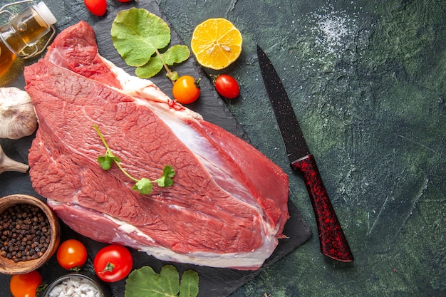 Vista superior de carne vermelha crua fresca em bandeja de pimenta preta de vegetais caídos faca de garrafa de óleo em fundo de cor escura