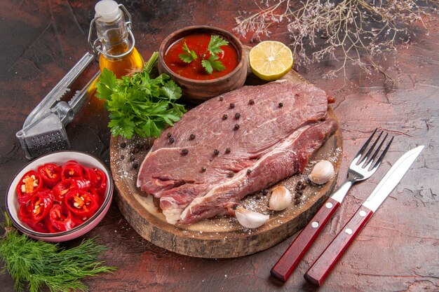 Vista superior de carne vermelha em uma bandeja de madeira e ketchup verde de alho e garrafa de óleo de pimenta picada em fundo escuro
