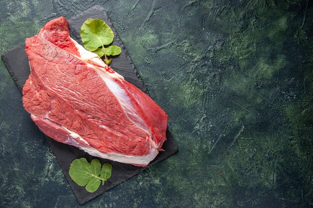 Vista superior de carne vermelha fresca crua e folhas na tábua de corte no lado direito sobre fundo verde preto mix de cores