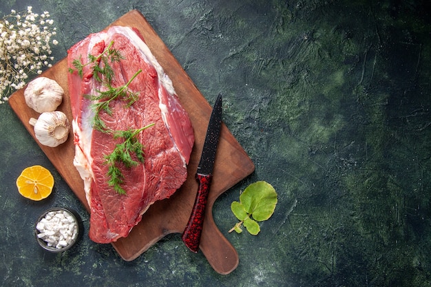 Vista superior de carnes vermelhas crus frescas faca de alho verde na tábua de madeira marrom sal limão no lado direito sobre fundo de cor escura