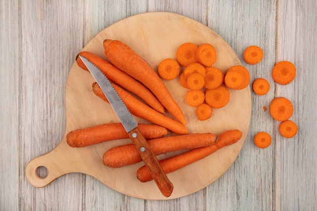 Vista superior de cenouras alimentícias para perda de peso em uma placa de cozinha de madeira com uma faca com cenouras picadas em um fundo cinza de madeira