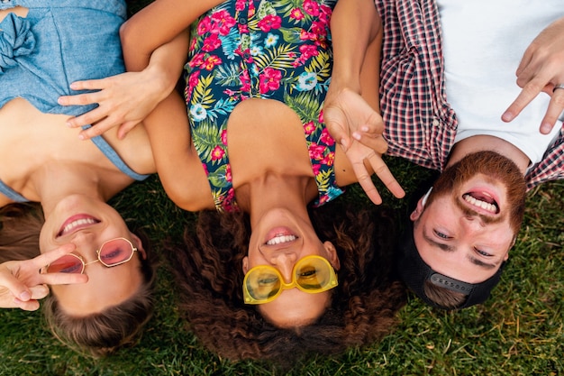 Vista superior de cima em colorida elegante feliz jovem companhia de amigos deitados na grama no parque, homens e mulheres se divertindo juntos