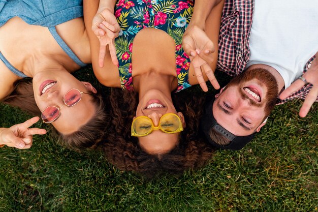 Vista superior de cima em colorida elegante feliz jovem companhia de amigos deitados na grama no parque, homens e mulheres se divertindo juntos