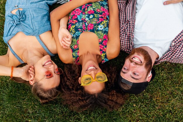 Vista superior de cima em colorida elegante feliz jovem companhia de amigos deitados na grama no parque, homens e mulheres se divertindo juntos