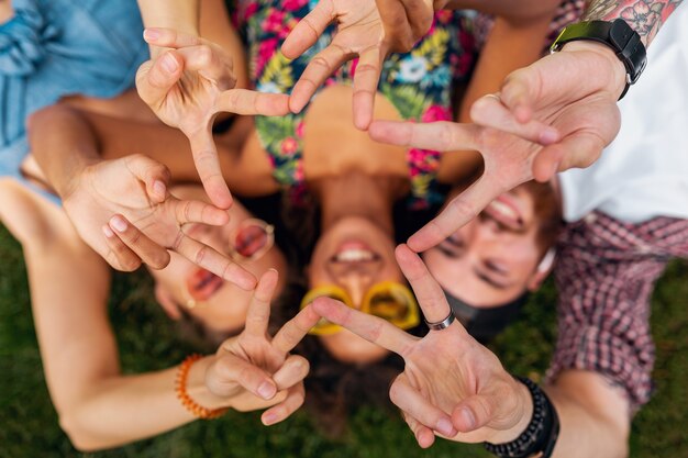 Vista superior de cima em colorida elegante feliz jovem companhia de amigos deitados na grama no parque, homens e mulheres se divertindo juntos