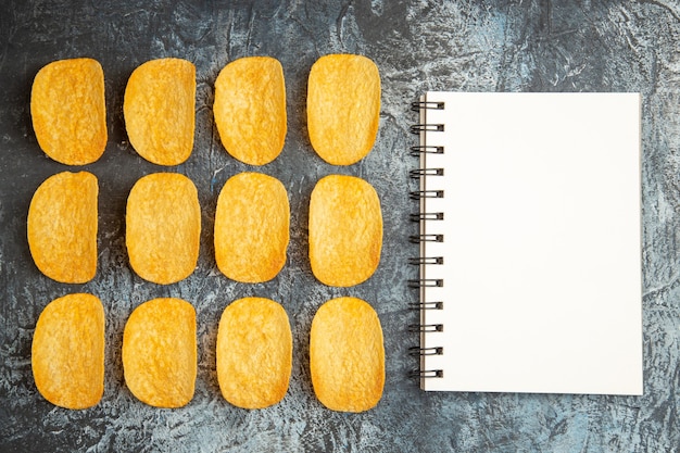 Vista superior de cinco chips assados crocantes alinhados em linhas e o caderno na mesa cinza