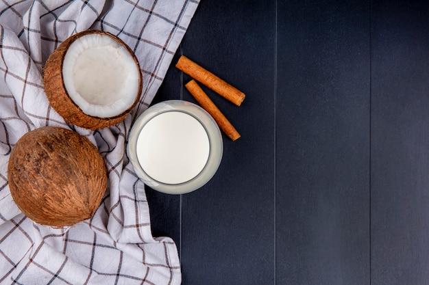 Vista superior de cocos com um copo de leite com paus de canela em toalha de mesa quadriculada em preto com espaço de cópia