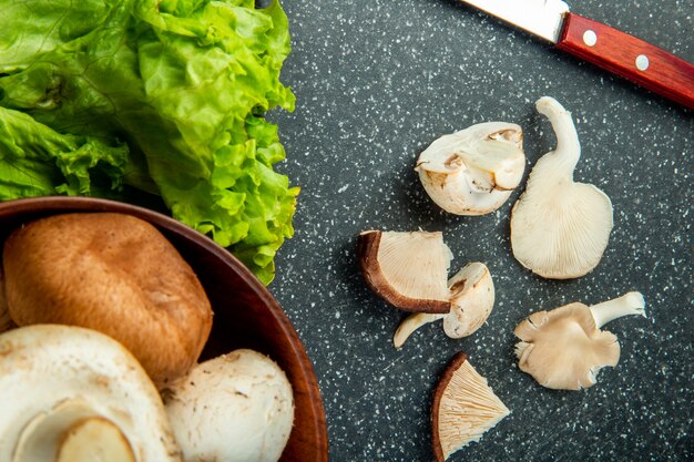 Vista superior de cogumelos fatiados com alface e faca de cozinha no quadro negro