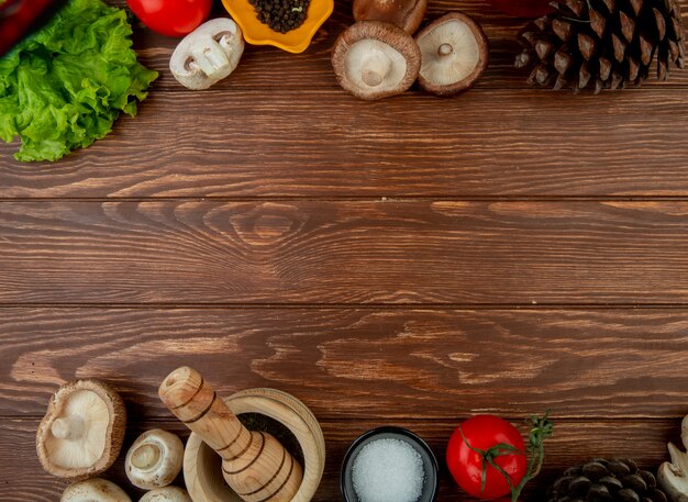 Vista superior de cogumelos frescos com pimenta preta, tomate fresco, almofariz de madeira com ervas secas sal e cones em madeira rústica, com espaço de cópia