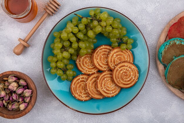 Vista superior de cookies com uvas verdes em um prato azul com mel e botões secos em um fundo branco