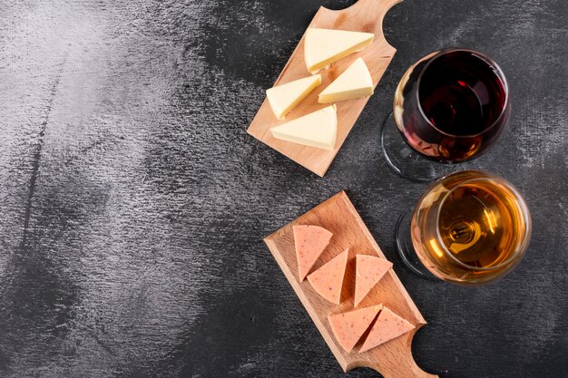 Vista superior de copos de vinho e queijo na tábua de madeira e copie o espaço no fundo escuro horizontal