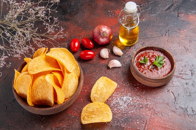 Vista superior de deliciosas batatas fritas caseiras crocantes, dentro e fora de uma garrafa de óleo de maconha marrom, tomate, alho, cebola, em fundo escuro