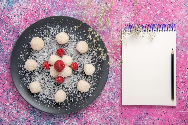 Vista superior de deliciosas bolas de doces de coco com bloco de notas na superfície rosa