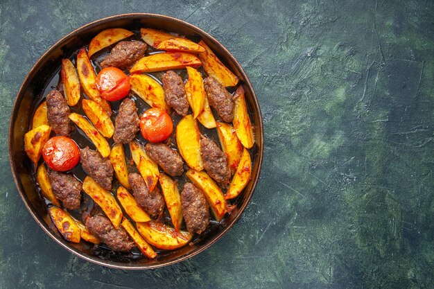 Vista superior de deliciosas costeletas de carne assadas com batatas e tomates no lado direito sobre fundo de cor verde e preto misturado