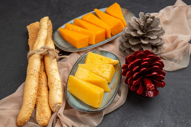 Vista superior de deliciosas fatias de queijo e cones de coníferas em uma toalha em um fundo preto