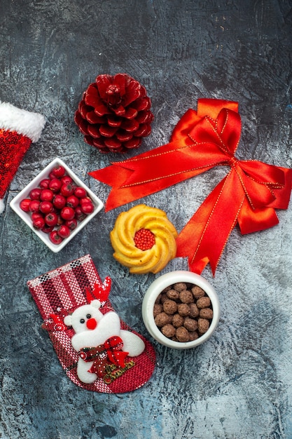 Foto grátis vista superior de deliciosos biscoitos e cornel em um prato branco meia conífera vermelha cone cone de fita vermelha chapéu de papai noel na superfície escura