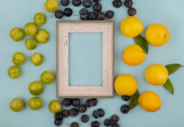 Vista superior de deliciosos pêssegos amarelos frescos com ameixas cereja verdes com abrunhos isolados em um fundo azul com espaço de cópia