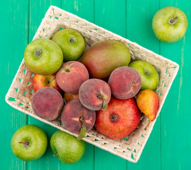 Vista superior de diferentes frutas, como pêssego, manga, pêra, romã, no balde, com maçãs verdes no verde