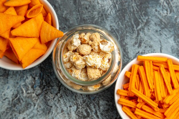 Vista superior de diferentes salgadinhos de pipoca tostas e cips na superfície escura