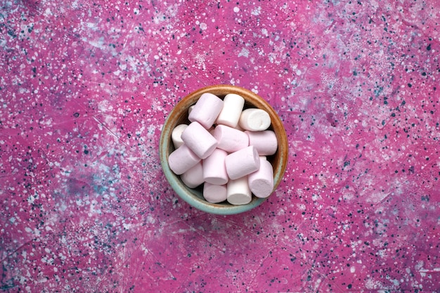 Vista superior de doces deliciosos marshmallows pouco formados dentro de uma panela redonda na superfície rosa