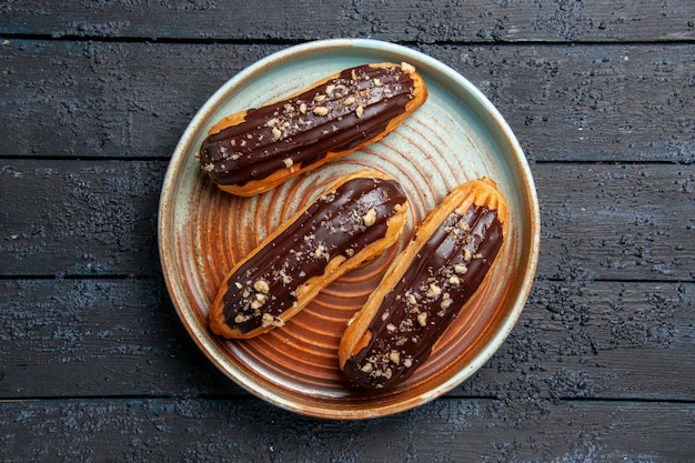 Vista superior de éclairs de chocolate em prato oval na mesa de madeira escura com espaço livre