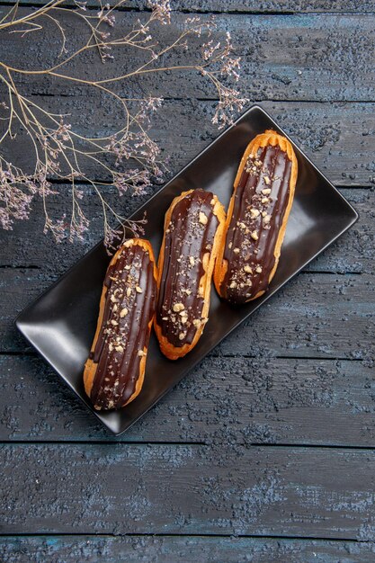 Vista superior de éclairs de chocolate em uma placa retangular escura na mesa de madeira escura com espaço livre